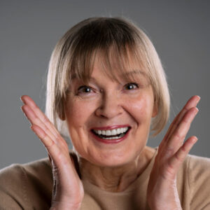 imagem de uma mulher idosa sorrindo com as mãos perto do rosto